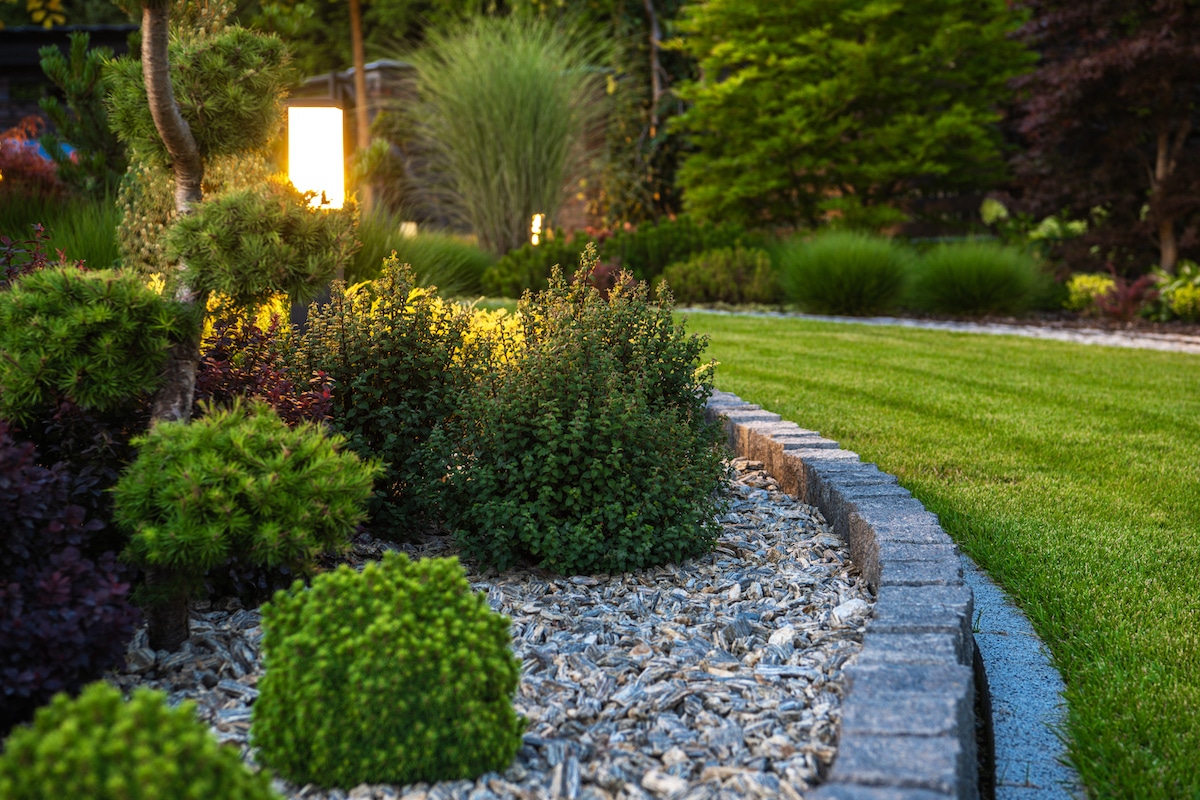 Modern Illuminated by LED Light Posts Backyard Garden. Decorative Plants and Small Residential Architecture.